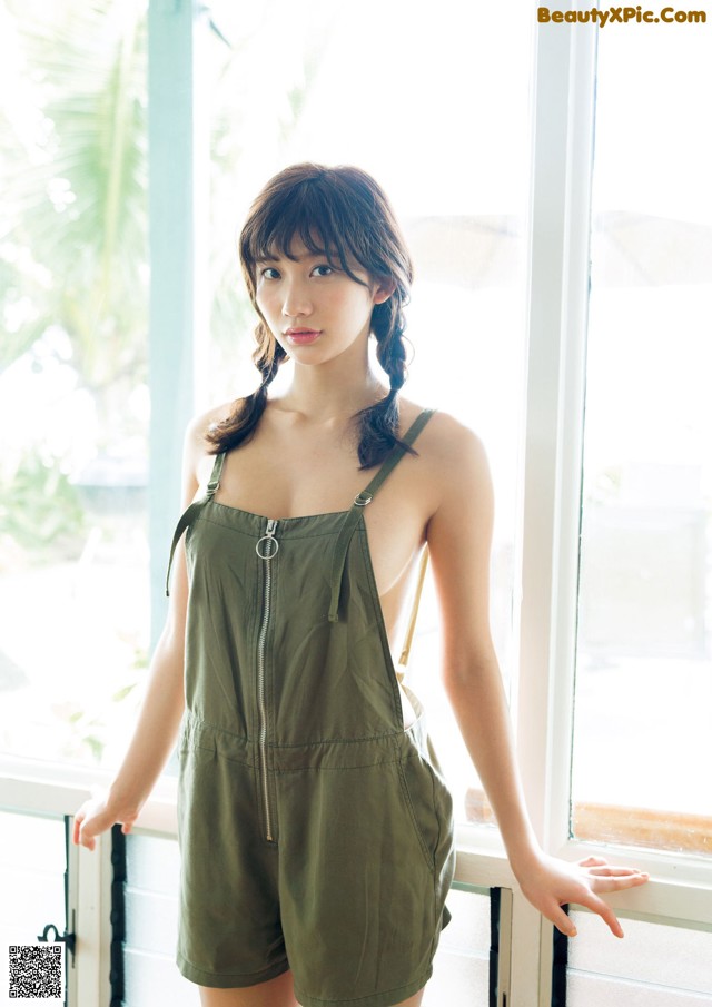A woman standing by a window wearing a green romper.
