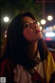 A woman with long brown hair standing in front of a city at night.