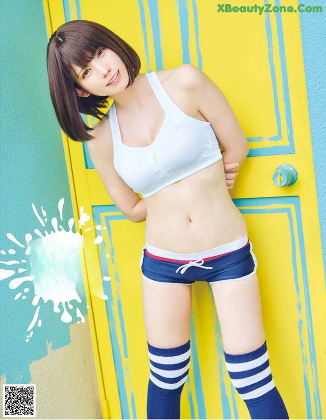A woman in a white top and blue shorts posing in front of a yellow door.
