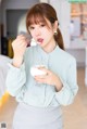 A woman holding a glass of milk and a spoon.