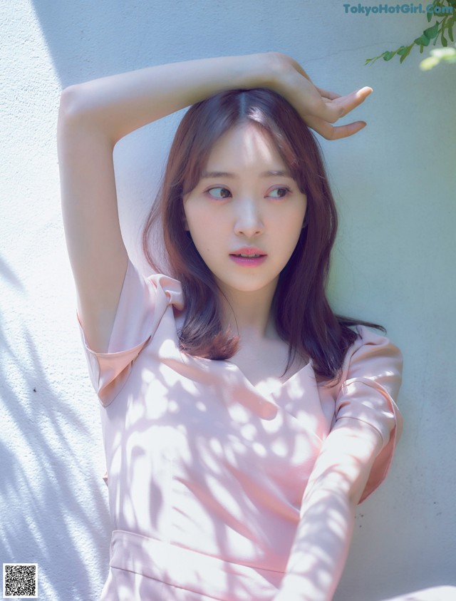 A woman in a pink dress leaning against a wall.