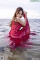 A woman in a red dress is sitting in the water.