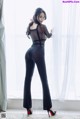 A woman in a black bodysuit leaning against a window.