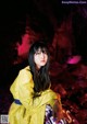 A woman in a yellow raincoat sitting on a rock.