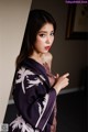 A woman in a purple and white kimono leaning against a wall.