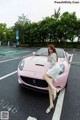 A woman sitting on top of a pink sports car.