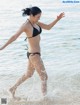 A woman in a black bikini running into the ocean.