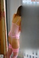 A woman in a pink lingerie standing by a window.