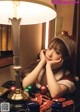 A woman in a santa hat sitting at a table next to a lamp.